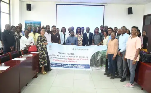 group photo in a conference room. There is a projector and the group together holds a sign that in French reads "Talks with professionals on the Congo Basin" with a Pulitzer Center logo.
