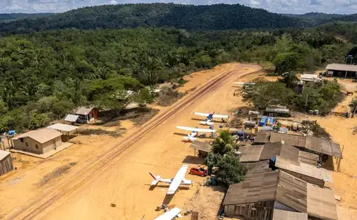 A view from above of an airstrip filled with small planes, carved out of the Amazon rainforest