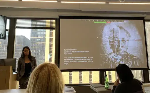Zalcman stands next to presentation screen with work on Indigenous communities.