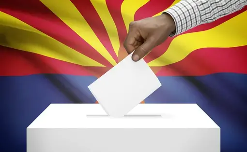 Stock image of hand dropping ballot into box in front of Arizona flag