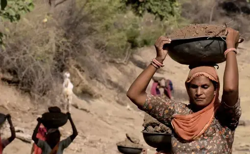 A woman laborer carries a large bowl of dirt above her head.