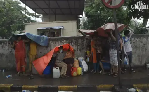 migrants in India huddle under a tarp to stay out of the rain
