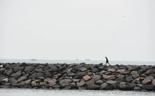 a man walks along a rocky shore on the water, India