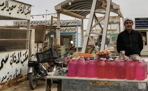 A man stands behind a table stacked with jugs of water, Iraq
