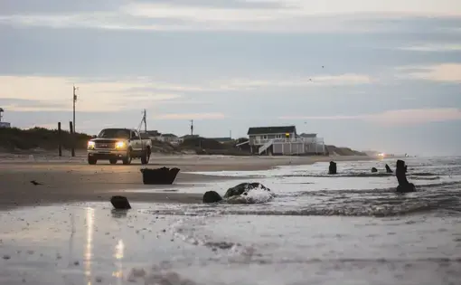 A truck with bright headlights trundles along a dusky ocean shore