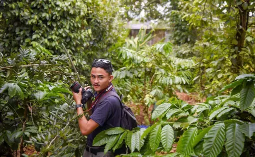 Anton Delgado stands in a forest holding a camera.