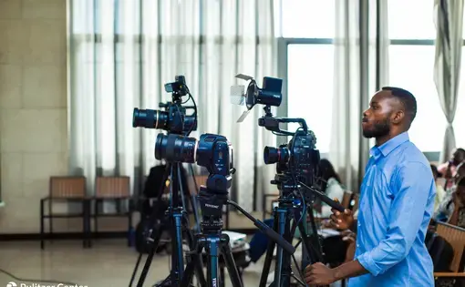 A person stands behind three live broadcast video cameras