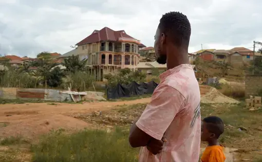 A man and his boy look up at a home built by a miner in the Western Region of Ghana.