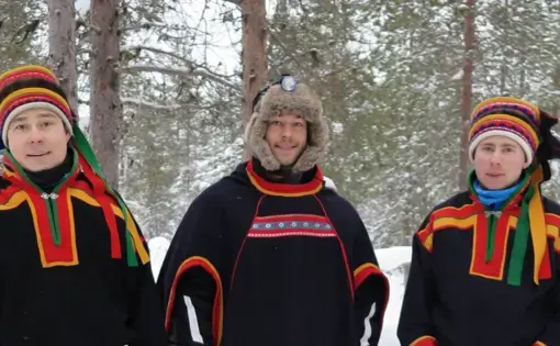 Three people in red-trimmed black dress stand in the snow