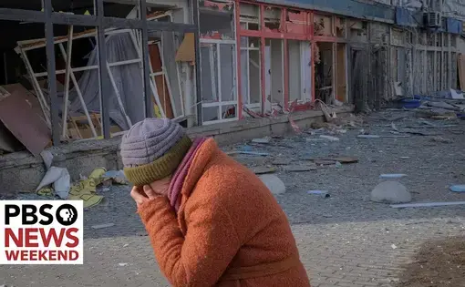 A person walks with their face in their hands through an area where a building was destroyed.