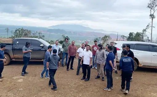 A group of men stand around cars on a dirt road.