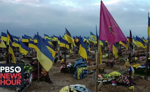 A field of freshly-dug graves with Ukrainian flags and flowers atop each gravesite.