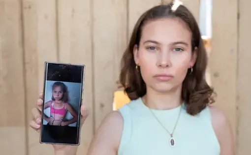 Environmental justice activist Nalleli Cobo stands at the gates of the now-shuttered Los Angeles AllenCo Energy site, holding a photo of herself as a child
