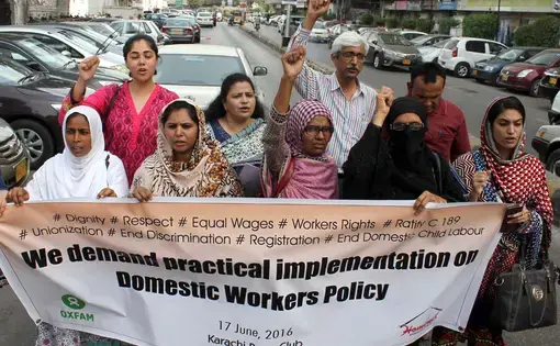 People hold up a protest sign: "We demand practical implementation on Domestic Workers Policy"