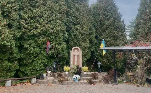 n Stradch, Ukraine, a cross is flanked by the national flag of Ukraine, right, and the flag of the Ukrainian Insurgent Army, left. The latter’s colors represent those of the first as if covered in blood. Image by Madeleine Long. Ukraine, 2022.