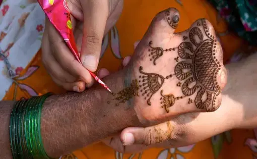 A henna artist paints the hand of a leprosy patient, whose disease has diminished their fingers.