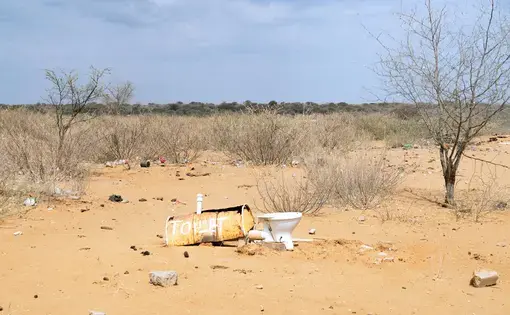 A makeshift toilet sits in an open field, surrounded by bone-dry vegetation.