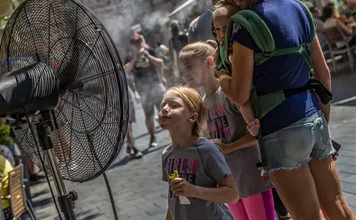 Unidentified people alleviate the summer heat wave in front of the water spraying fan at the street of downtown.