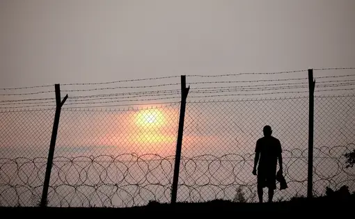 Silhouette of a prisoner behind a barbed wire fence in a concentration camp against fiery setting sun.