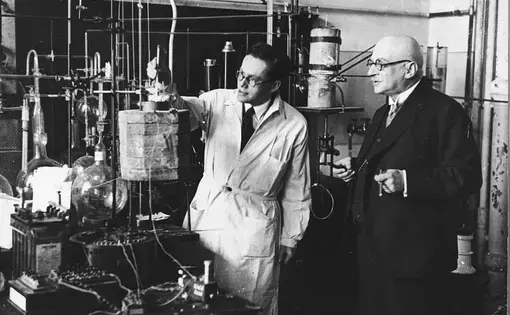 Three scientists observe a chemical experiment; black and white archival photo.