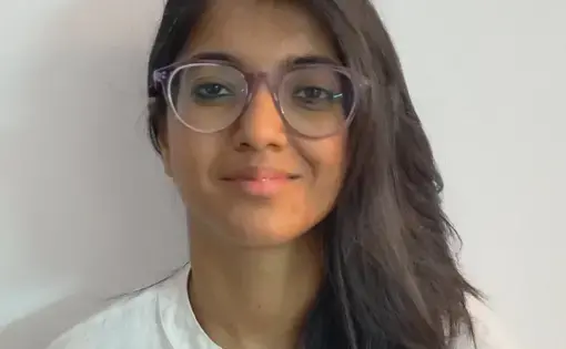 A woman with medium length hair and brown skin wearing a white shirt stands with a white background
