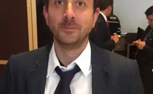 A headshot of a man in a suit and tie with short dark hair