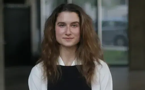 A woman with long light hair wears a white shirt with black overalls