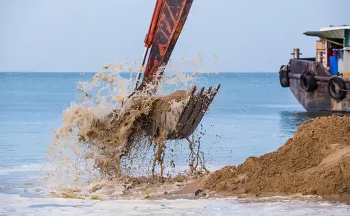 a mechanical arm shovels sand