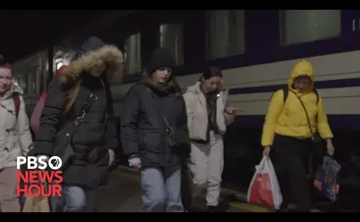 A group of women in winter coats walk alongside a train in Ukraine