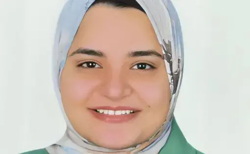 A woman smiles at the camera wearing a grey hijab and a green shirt