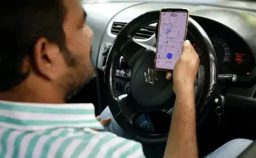 An uber driver checks the map on his phone while sitting at the wheel.