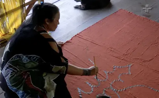 A woman perches on the floor absorbed in intricate handcraft.