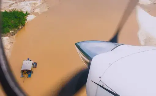 An aerial image of a dredge on a river. The propeller of the plane is in the foreground.