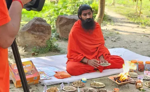 A man in orange robes sits crossed legged on the ground