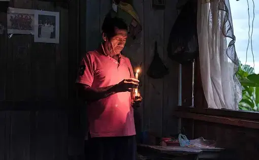 A man in pink t-shirt lights a candle.