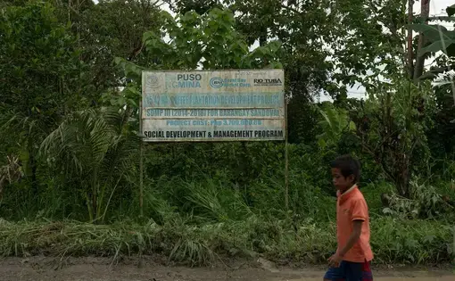 A boy in orange walks by a green sign board.