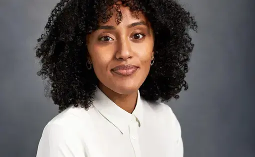 A woman with dark curly hair wearing a white button down shirt
