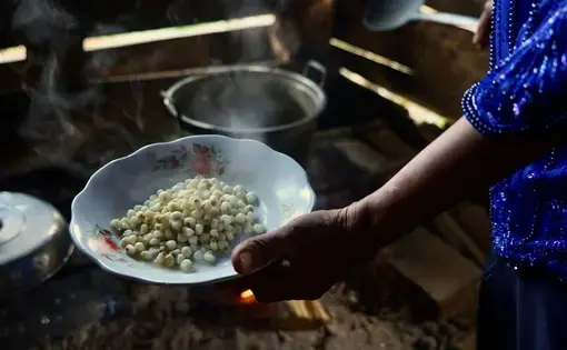 A hand holds a plate full of white old corn with steam rising.
