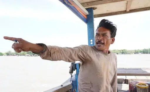 A fisherman points to his right in a boat.