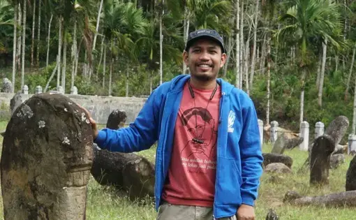 A man is smiling wearing a red shirt and blue jacket.
