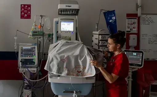 A nurse in red scrubs tends to a newborn's incubator
