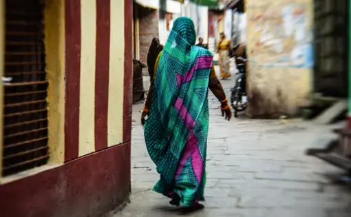 A woman in a sari walks away from the camera down a narrow street