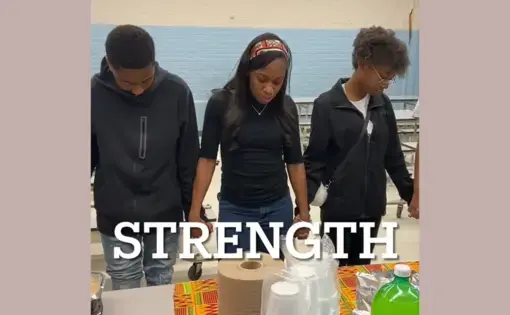 Students hold hands and bow their heads around a table spread with food. The word "strength" appears in bold letters.