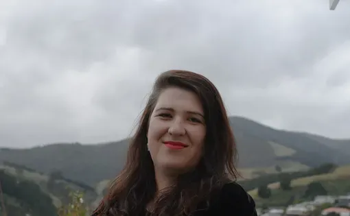 A woman with long dark hair smiles against a mountainous background