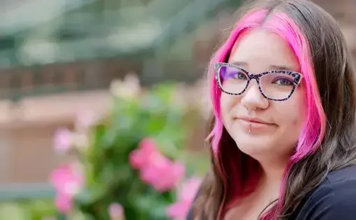 A woman with glasses and long dark hair with pink dyed streaks
