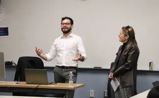 Man in white shirt gestures to class next to woman in black jacket