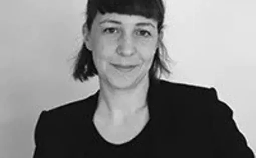 A woman with short dark hair and bangs wearing a black top and blazer