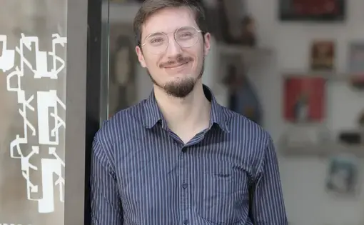 a man with short dark hair, short beard, and glasses wearing a blue button down