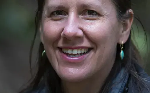 A woman with long dark hair wearing earrings and a jacket