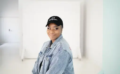 A woman wearing a black "Basquiat" baseball cap and a jean jacket